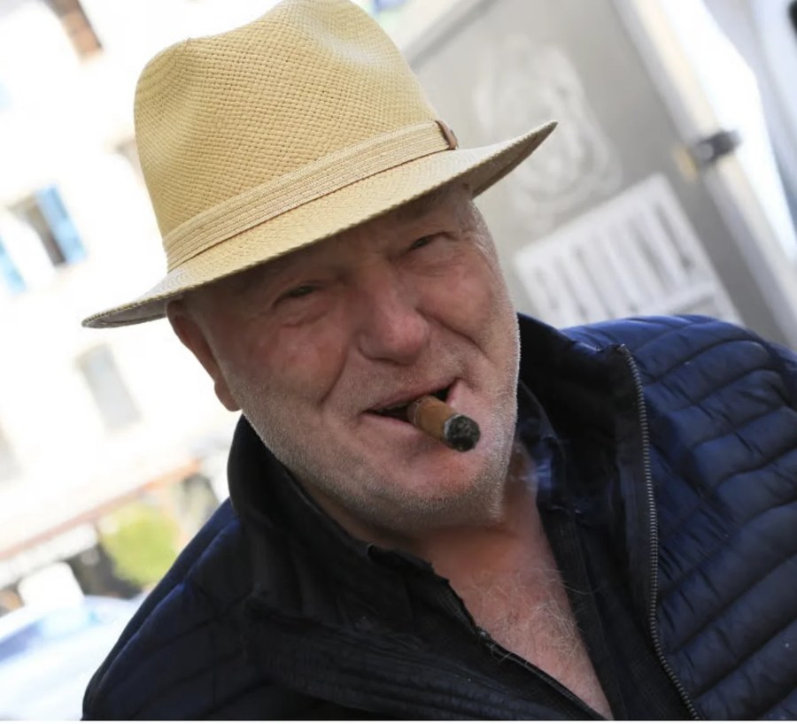 Manu Simonini, souriant, chapeau de paille et cigare aux lèvres, devant la vieille cave de Corte.